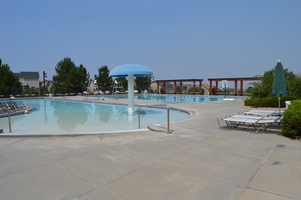 Outdoor pool area with a blue mushroom-shaped water feature in the children's pool, lounge chairs, and a large umbrella.