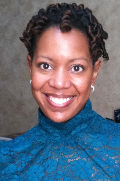 Brooke, a woman with black curly hair, smiling in a teal lace blouse.

