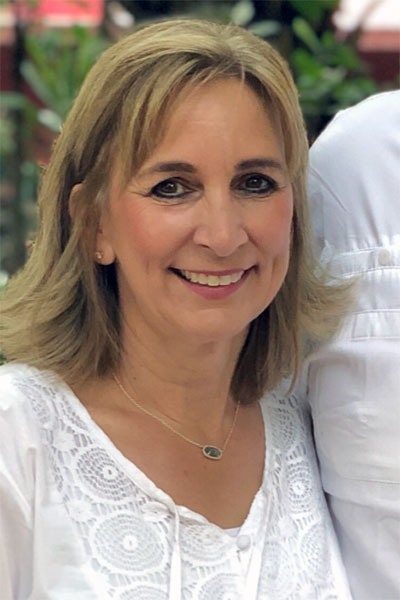 Polly Martin, a woman with blonde hair, wearing a white embroidered shirt and smiling.