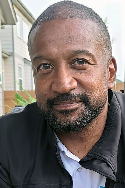 Rodney, with a dark short beard, smiling in a white shirt and black jacket.