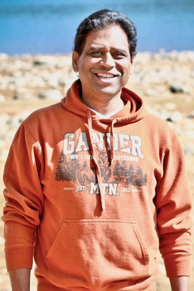 Sameer, a man with black hair, smiling while wearing an orange hoodie in an outdoor setting.
