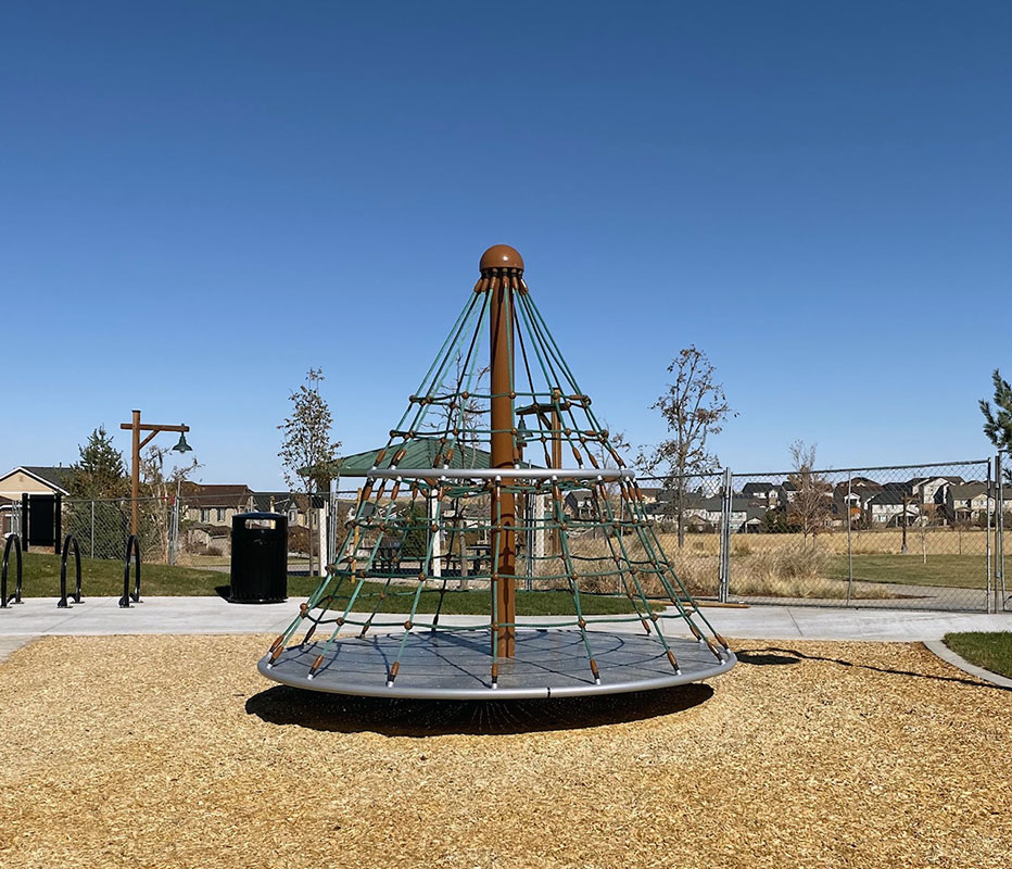 A playground with a cone-shaped rope climbing structure and wood chip surface.