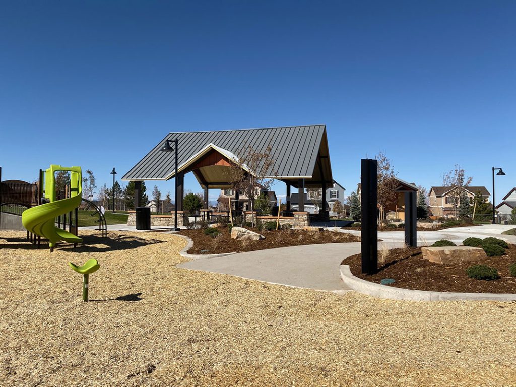 A vibrant park with a green spiral slide, pavilion, and residential homes in the background.