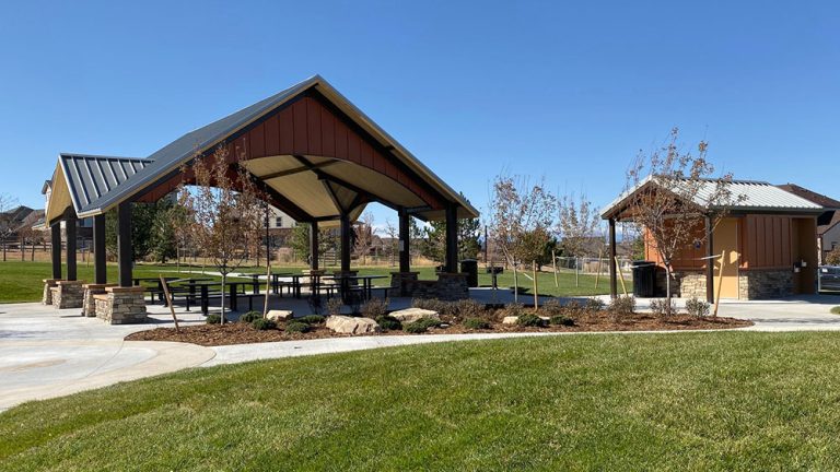 Wheatlands main park pavilion with picnic tables, flanked by a small utility building and landscaped greenery.